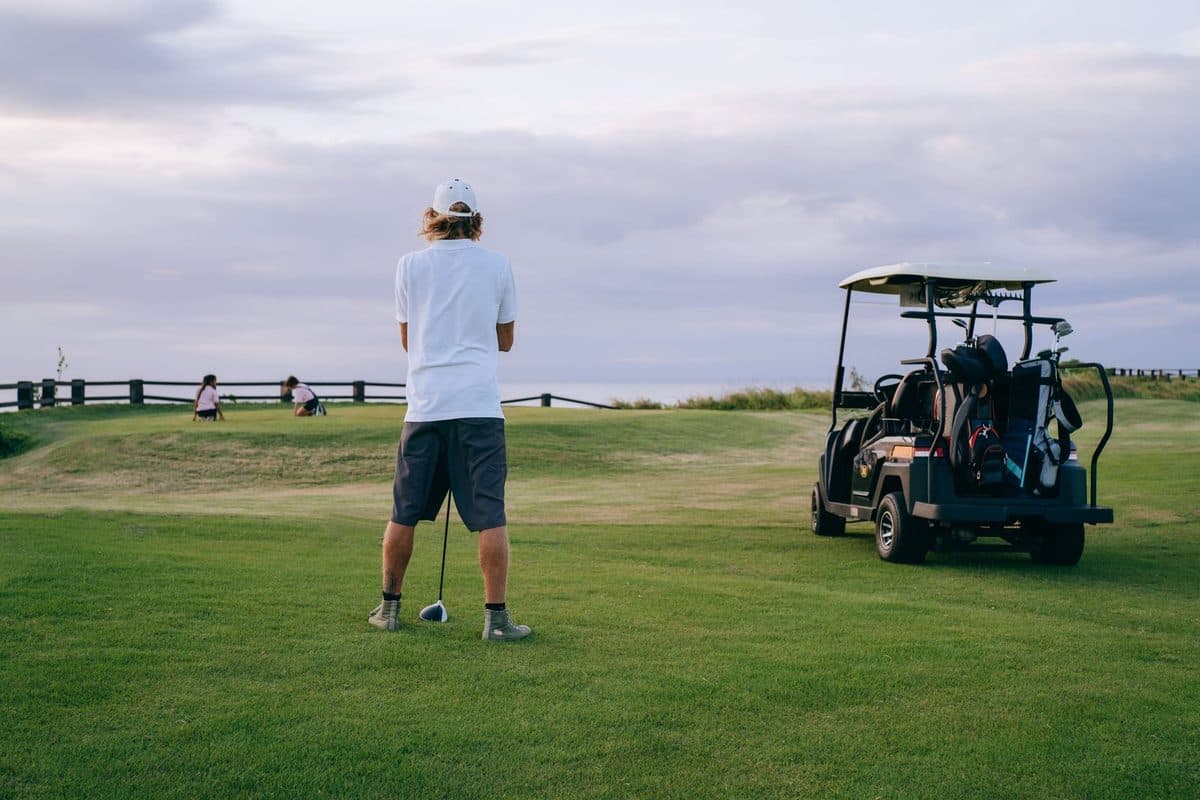 Golfer standing on the tee with a driver beside a golf buggy on a UK course